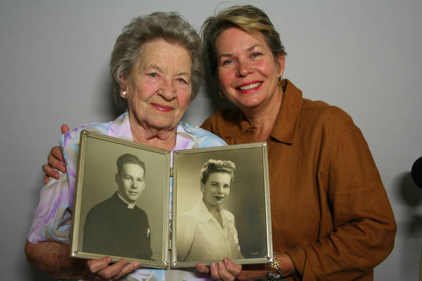 Elderly mother and adult daughter smiling with old family photo between them