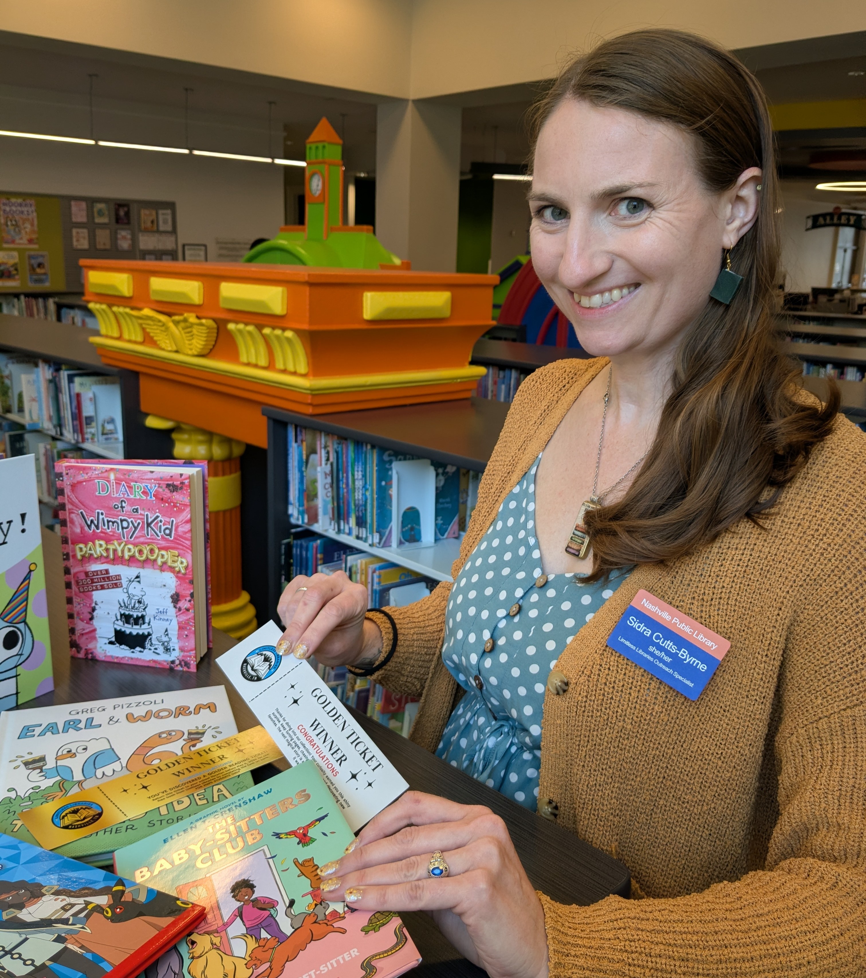 Woman holding reading prize, standing next to a display of kids books.