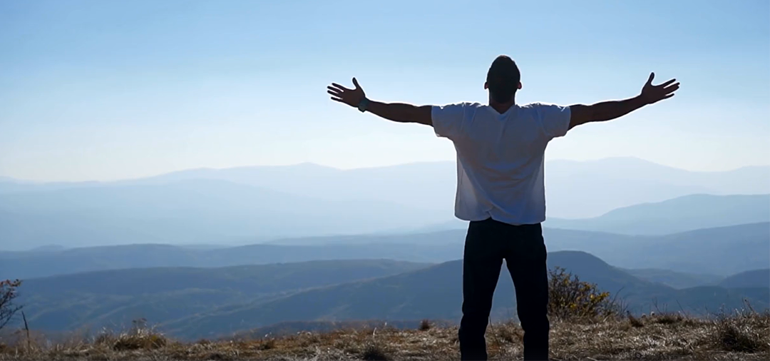 freedom concept: man with open arms facing mountain view