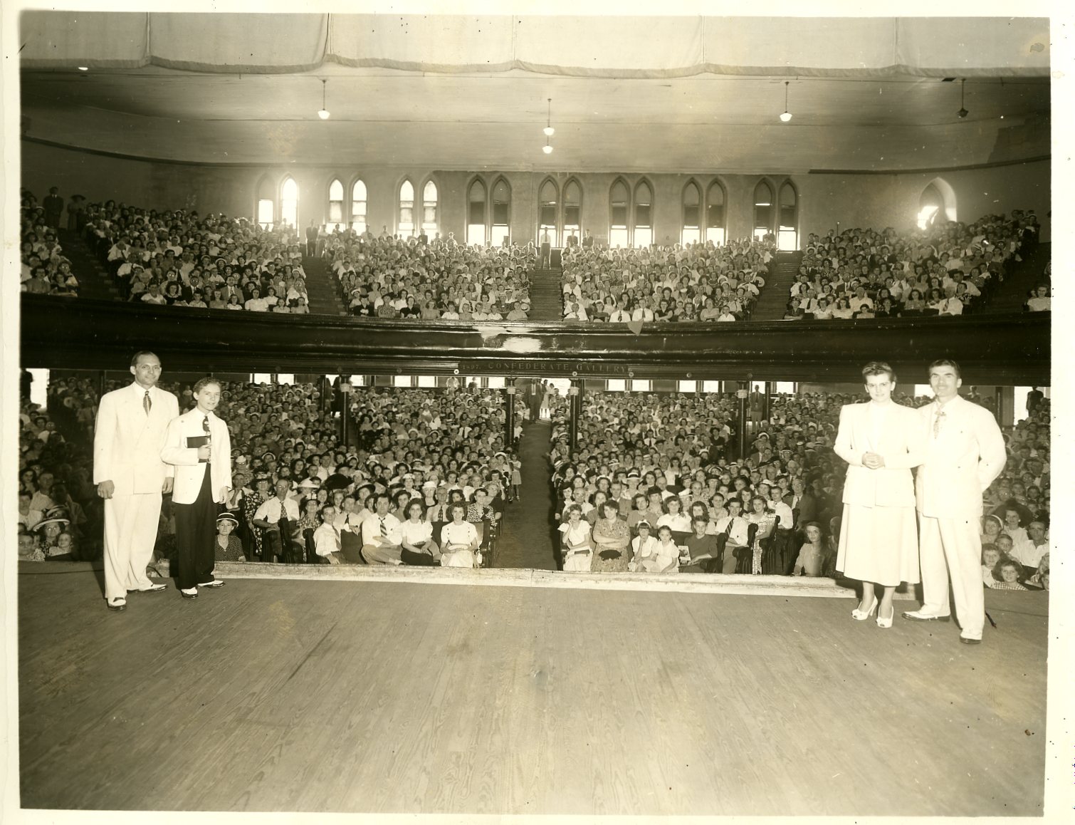 View of the Ryman Auditorium with people on stage and the crowd facing the camera