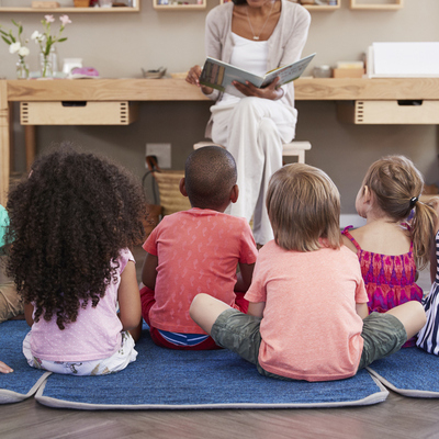 Woman reading to a group of children sitting on the floor, backs to us
