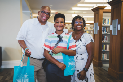 Photo of man, woman, and teenage boy standing inside the Main Library near bookshelves.
