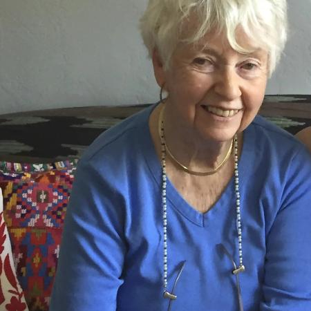 Author Eve Bunting. Photo shows an older white woman with short white hair, wearing a long sleeved blue shirt and a long chain around her neck.