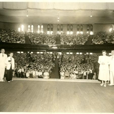 View of the Ryman Auditorium with people on stage and the crowd facing the camera